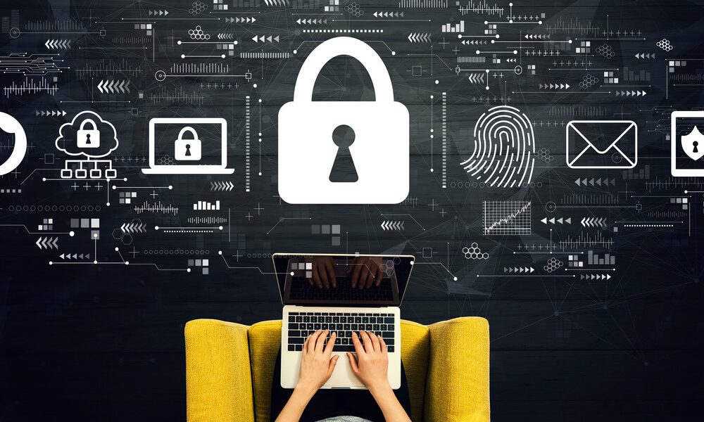 Person typing on a laptop on a yellow chair, with large padlock and digital security icons floating above, illustrating cybersecurity.