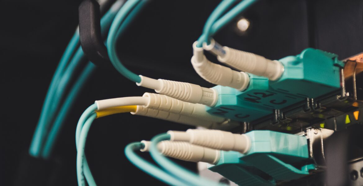 Close-up of teal Ethernet cables plugged into a network patch panel in a server rack, dimly lit.