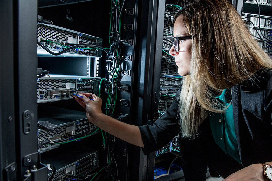 Female IT technician in a data center plugs a network cable into a rack-mounted server.
