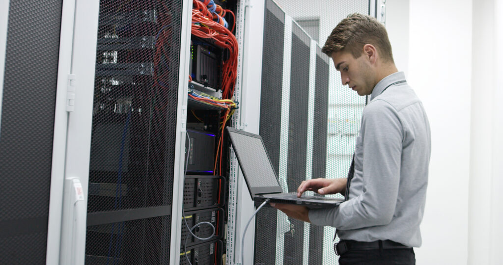 IT technician using a laptop to configure servers in a data center cabling room